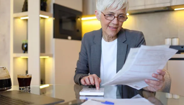 Foto de una mujer en una mesa, sosteniendo papeles y usando una calculadora.